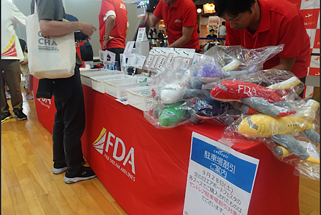 FDAの公式事例に掲載されたイベントブース。飛行機のぬいぐるみなどのオリジナルグッズが並ぶ。